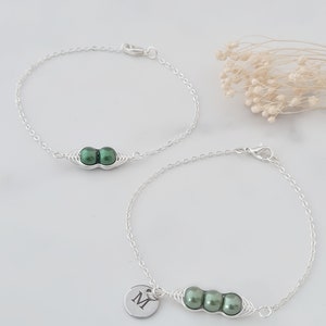 May include: Two silver-toned chain bracelets featuring wire-wrapped green beads. One bracelet contains two beads, while the other features three beads and a small round silver charm engraved with the capital letter M, both with lobster clasps.