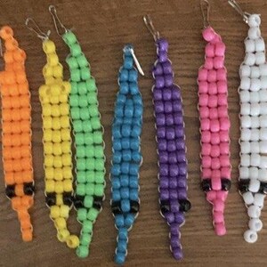 May include: A collection of colorful beaded keychains in various colors, including red, orange, yellow, green, blue, purple, pink, white, and black. Each keychain features a small metal clasp for attachment.