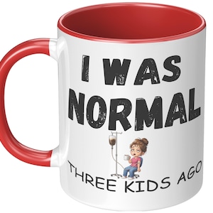 May include: White ceramic mug with a red interior and handle. The mug features the text "I WAS NORMAL THREE KIDS AGO" in black, with an illustration of a tired person hooked up to an IV drip.