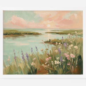 Op de afbeelding: Een ingelijst landschapsschilderij met een serene kustscène bij zonsondergang. Het kunstwerk toont een kalm wateroppervlak dat een zachte roze en perzikkleurige lucht weerspiegelt, met groen moerasland en een voorgrond vol witte, roze en paarse bloemen.