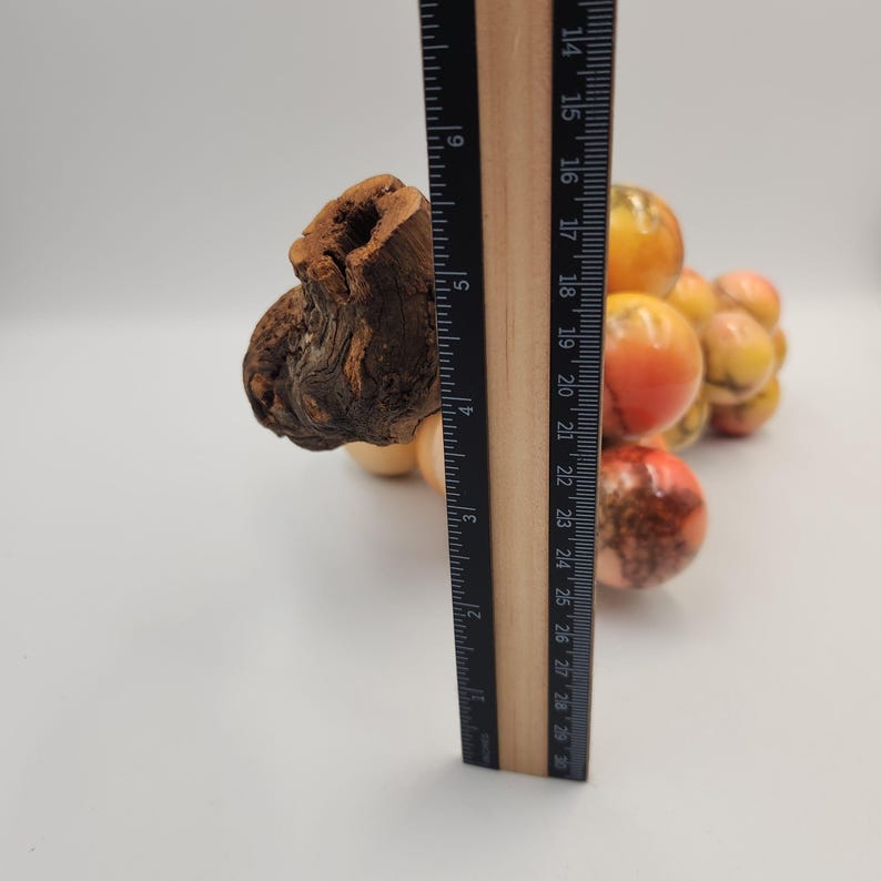 May include: A wooden sculpture of a cluster of grapes with a wooden stem. The grapes are in shades of orange, red, and yellow. A ruler is placed next to the sculpture, showing a height of approximately 9 inches.