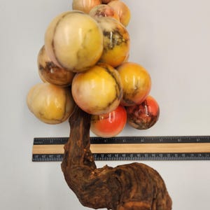 May include: A decorative sculpture of a cluster of marble spheres in shades of yellow, orange, and red, attached to a natural wood base. The spheres vary in size and have unique veining patterns. A ruler is placed next to the sculpture.