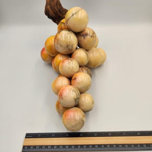 May include: A decorative cluster of marble grapes with a wooden stem. The grapes are a mix of cream, yellow, and orange hues, with subtle veining. The ruler shows the grapes are approximately 10 inches long.