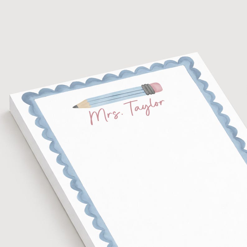 May include: A white notepad with a scalloped light blue border. The top center features a horizontal light blue pencil illustration with a pink eraser and a dark gray ferrule. Below the pencil, the text Mrs. Taylor is printed in pink.