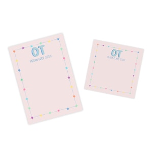 Puede incluir: Dos blocs de notas rosas con un borde de estrellas de colores. El bloc de notas superior tiene las letras "OT" en azul, con el nombre "Megan Grey OTR/L" debajo. El bloc de notas más pequeño tiene las letras "OT" en azul, con el nombre "Olivia Clare OTR/L" debajo.