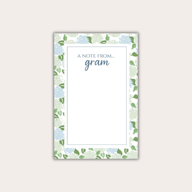 May include: A rectangular notepad with a white interior and a floral border. The border features light blue and green hydrangea blooms and leaves on a white background. The text "A NOTE FROM... gram" is printed at the top.