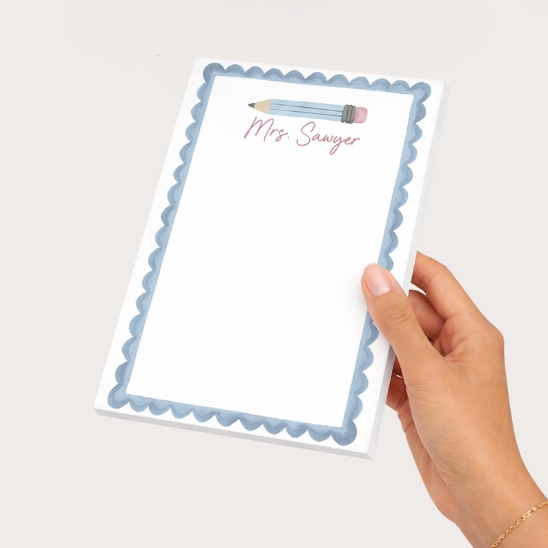 May include: A rectangular notepad with a white center and a scalloped blue border. The top of the page features a watercolor illustration of a light blue pencil and the text Mrs. Sawyer printed in a cursive pink font on the white background.