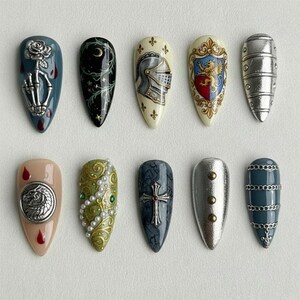 Pu&ograve; includere: Una collezione di dieci unghie finte a forma di mandorla con disegni dettagliati. Le unghie presentano vari temi, tra cui una mano di scheletro con una rosa, un elmo da cavaliere e una croce d'argento. Le unghie sono dipinte in vari colori.