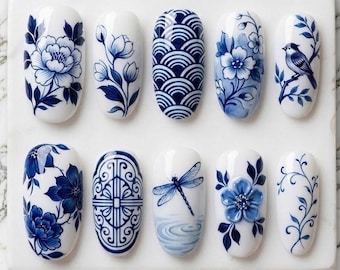 Può includere: Dieci unghie finte bianche con intricati disegni blu, tra cui fiori, un uccello e una libellula. I disegni sono in blu e bianco, che ricordano la porcellana tradizionale. Le unghie sono esposte su una superficie bianca.