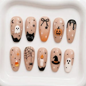 Peut inclure: Un ensemble de dix faux ongles en amande sur base nude, arborant des motifs d'Halloween incluant un fantôme blanc, un chat noir, une citrouille, une toile d'araignée, une bougie, un chapeau de sorcière, un bonbon, un nœud et des gouttes noires.