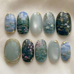 Puede incluir: Un conjunto de diez uñas postizas ovaladas. Cada uña presenta un diseño único, incluyendo nenúfares, puentes y paisajes, con detalles dorados. La paleta de colores incluye azules, verdes y rosas, creando una estética serena y artística.