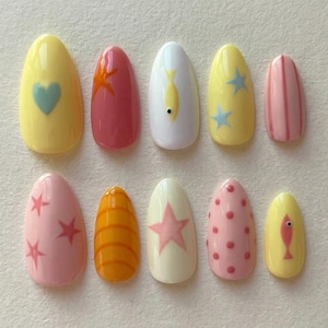 May include: A set of ten almond-shaped press-on nails featuring various designs including a light blue heart on yellow, a starfish on pink, a yellow fish on white, blue stars on yellow, pink stripes, pink stars on pink, orange stripes, a pink star on cream, pink dots, and a pink fish on yellow.
