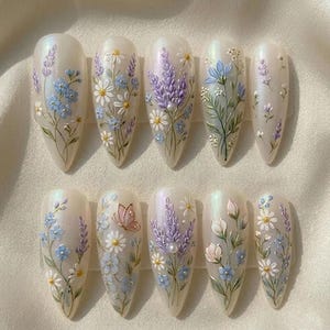 May include: A set of ten almond-shaped artificial nails, each adorned with delicate floral designs. The nails feature a pearlescent base with hand-painted details of lavender, daisies, and blue flowers, some with a butterfly accent.