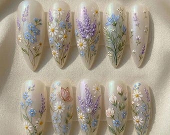 May include: A set of ten almond-shaped artificial nails, each adorned with delicate floral designs. The nails feature a pearlescent base with hand-painted details of lavender, daisies, and blue flowers, some with a butterfly accent.
