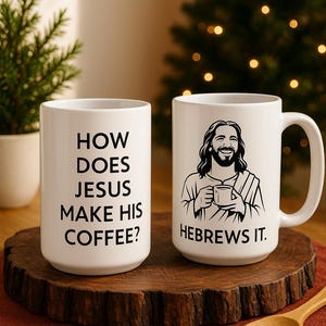 May include: Two white ceramic coffee mugs with black text and illustrations. One mug asks "HOW DOES JESUS MAKE HIS COFFEE?" The other mug says "HEBREWS IT." The mugs are on a wooden surface.
