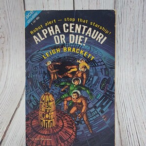 May include: Vintage paperback book titled "Alpha Centauri or Die!" by Leigh Brackett. The cover features a colorful illustration of astronauts in space suits, with the text "Robot alert - stop that starship!" printed above the title. Published by Ace.