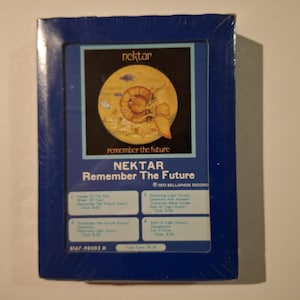 Peut inclure: Une cassette 8 pistes Nektar "Remember the Future" dans un cadre bleu. L'illustration de l'album présente une illustration jaune et marron d'un escargot sur une planète. Le texte "Nektar" et "Remember The Future" sont affichés à l'avant.