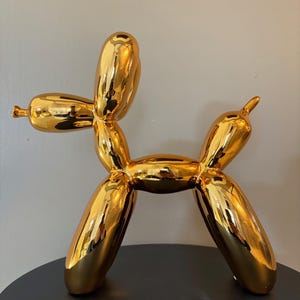 May include: A gold balloon animal sculpture in the shape of a dog. The sculpture is made of ceramic and has a shiny, metallic finish.