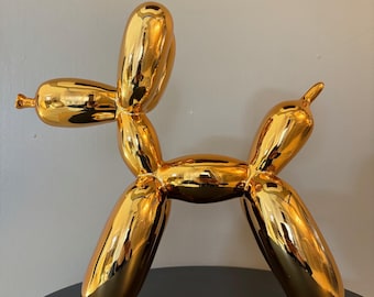 May include: A gold balloon animal sculpture in the shape of a dog. The sculpture is made of ceramic and has a shiny, metallic finish.