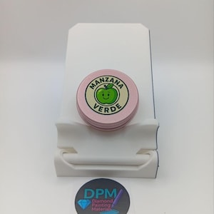 Puede incluir: Una pequeña lata redonda rosa con las palabras "MANZANA VERDE" y un gráfico de manzana verde. La lata está sobre un soporte blanco, con una pegatina debajo que dice "DPM Diamond Painting Materials".