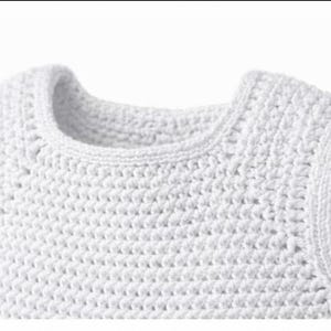 May include: A sleeveless top crafted from white yarn in a dense, uniform crochet stitch pattern. The garment features a rounded neckline and finished edges along the armholes and collar, showcasing a consistent, textured handmade construction.