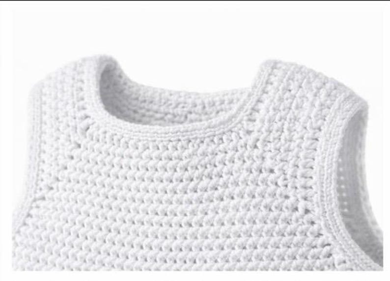 May include: A sleeveless top crafted from white yarn in a dense, uniform crochet stitch pattern. The garment features a rounded neckline and finished edges along the armholes and collar, showcasing a consistent, textured handmade construction.