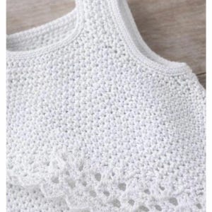 May include: A sleeveless white top featuring a dense crochet knit construction with a rounded neckline and a decorative scalloped edge detail that drapes across the chest, showcasing a uniform texture throughout the entire garment.