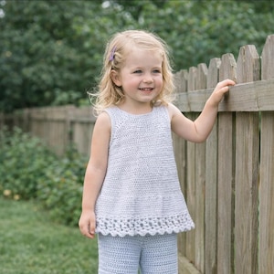 May include: A light blue sleeveless crochet top with a textured stitch pattern and a decorative scalloped hemline. The garment features a round neckline and a flared silhouette, crafted from a soft yarn material in a solid, uniform color.