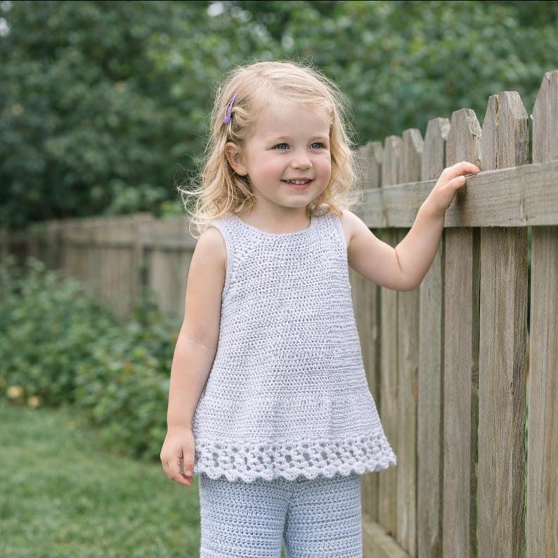 May include: A light blue sleeveless crochet top with a textured stitch pattern and a decorative scalloped hemline. The garment features a round neckline and a flared silhouette, crafted from a soft yarn material in a solid, uniform color.