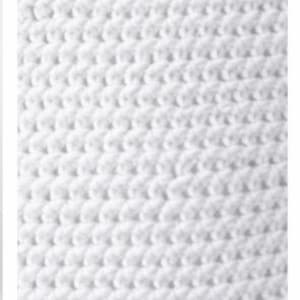 May include: A close-up view of a white textile featuring a consistent, repeating crochet stitch pattern. The surface displays a dense, textured arrangement of interconnected loops, creating a uniform and tactile appearance across the entire fabric.