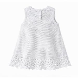 May include: A sleeveless white dress featuring a dense crochet knit pattern throughout the bodice and a decorative, openwork scalloped lace border along the hem. The garment includes a vertical placket at the upper back with three small buttons.
