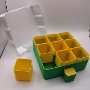 May include: A green and yellow plastic seed starting tray with a clear plastic lid. The tray has nine yellow square pots. One yellow pot and the lid are separate from the tray. The tray is designed for starting seeds indoors.