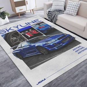 Könnte beinhalten: Ein rechteckiger Teppich mit einem blauen Nissan Skyline-Auto. Der Teppich zeigt das Wort "SKYLINE" in Blau und Weiß, mit "GTR" in Rot. Der Text "ANYONE, ANYTIME, ANYWHER" ist ebenfalls sichtbar. Der Teppich hat ein JDM-Logo.