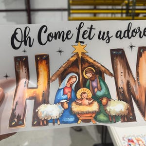 May include: A Christmas-themed graphic with the text "Oh Come Let us adore Him." The image depicts the Nativity scene with Mary, Joseph, baby Jesus, and sheep. The letters "HIM" are stylized with a brown and orange gradient.