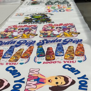 May include: Printed fabric with various designs, including text and illustrations. The designs feature phrases like "Everything's Fine," cartoon characters, and soda bottle graphics. The fabric is white with colorful prints.