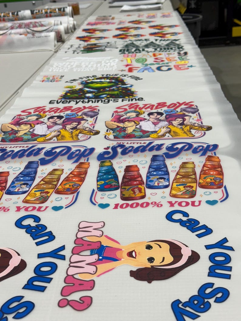 May include: Printed fabric with various designs, including text and illustrations. The designs feature phrases like "Everything's Fine," cartoon characters, and soda bottle graphics. The fabric is white with colorful prints.