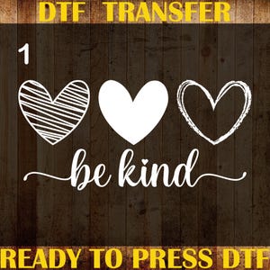 May include: A black and brown DTF transfer design featuring three white hearts and the words "be kind" in a script font. The design includes the text "DTF TRANSFER", "CUSTOM PRINT", "HEAT TRANSFER", and "READY TO PRESS DTF".