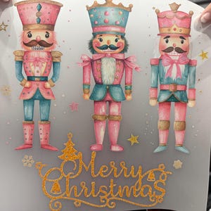 May include: A sheet featuring three watercolor-style nutcracker figures in pink and teal uniforms, each with a mustache and a tall hat. The words "Merry Christmas" are written in gold glitter.