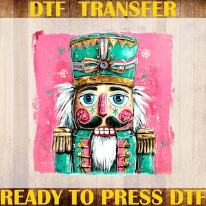 May include: A colorful DTF (Direct to Film) transfer featuring a whimsical nutcracker design. The nutcracker is depicted with a green and gold hat and jacket, a black mustache, and a white beard, set against a pink background. The text "DTF TRANSFER" and "READY TO PRESS DTF" are visible.