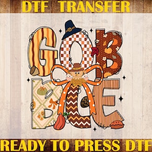 May include: DTF transfer design with the word "GOBBLE" in fall colors and patterns. The letters are decorated with pumpkins, acorns, and a turkey wearing a pilgrim hat. The text "READY TO PRESS DTF" is at the bottom.