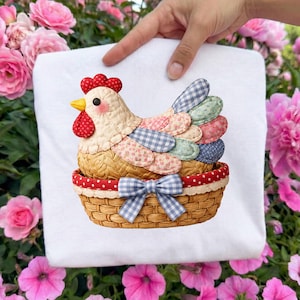 Könnte beinhalten: Weißer Stoff mit einer farbenfrohen Applikation einer Henne in einem Korb. Die Henne hat einen roten Kamm und Kehllappen, mit gemusterten Flügeln in Blau, Rosa und Grün. Der Korb ist mit rotem Tupfenbesatz und einer blau-weiß karierten Schleife gewebt.