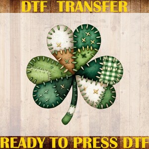 May include: A shamrock design with a patchwork effect in shades of green, tan, and white, with stitched details. The image includes the text "DTF TRANSFER", "CUSTOM PRINT", "HEAT TRANSFER", and "READY TO PRESS DTF".