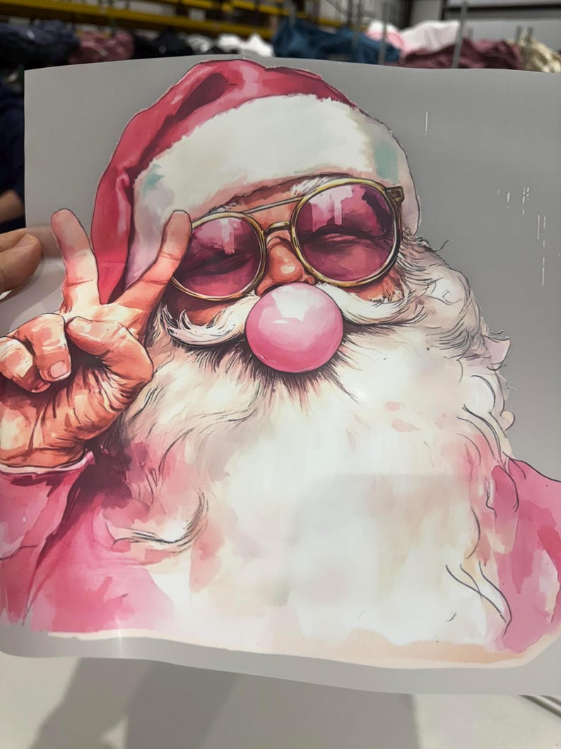 May include: A watercolour illustration of Santa Claus wearing sunglasses and a red hat, blowing a pink bubble. Santa is giving the peace sign with his left hand. The image has a whimsical and festive feel.
