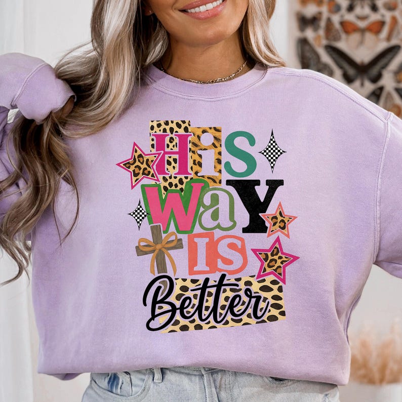 May include: A lilac sweatshirt featuring the text "His Way Is Better" in a layered design. The design incorporates leopard print, stars, and a cross.