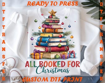 May include: White sweatshirt with a Christmas tree design made of books, ornaments, and a star. The text "ALL BOOKED FOR Christmas" is displayed below the tree. The words "READY TO PRESS" and "CUSTOM DTF PRINT" are also visible.