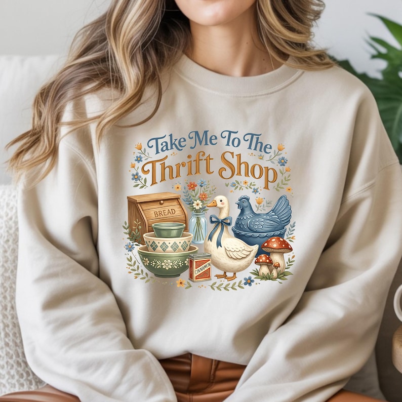 May include: Beige sweatshirt with a graphic that says "Take Me To The Thrift Shop." The graphic features a bread box, bowls, a duck with a blue bow, a blue chicken, mushrooms, and flowers.