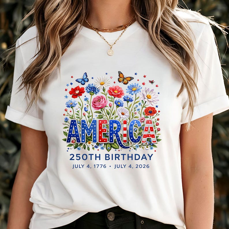 K&ouml;nnte beinhalten: Wei&szlig;es T-Shirt mit floralem Design und dem Wort "AMERICA" in Rot, Wei&szlig; und Blau. Das Design umfasst Blumen, Schmetterlinge und den Text "250TH BIRTHDAY JULY 4, 1776 &bull; JULY 4, 2026".