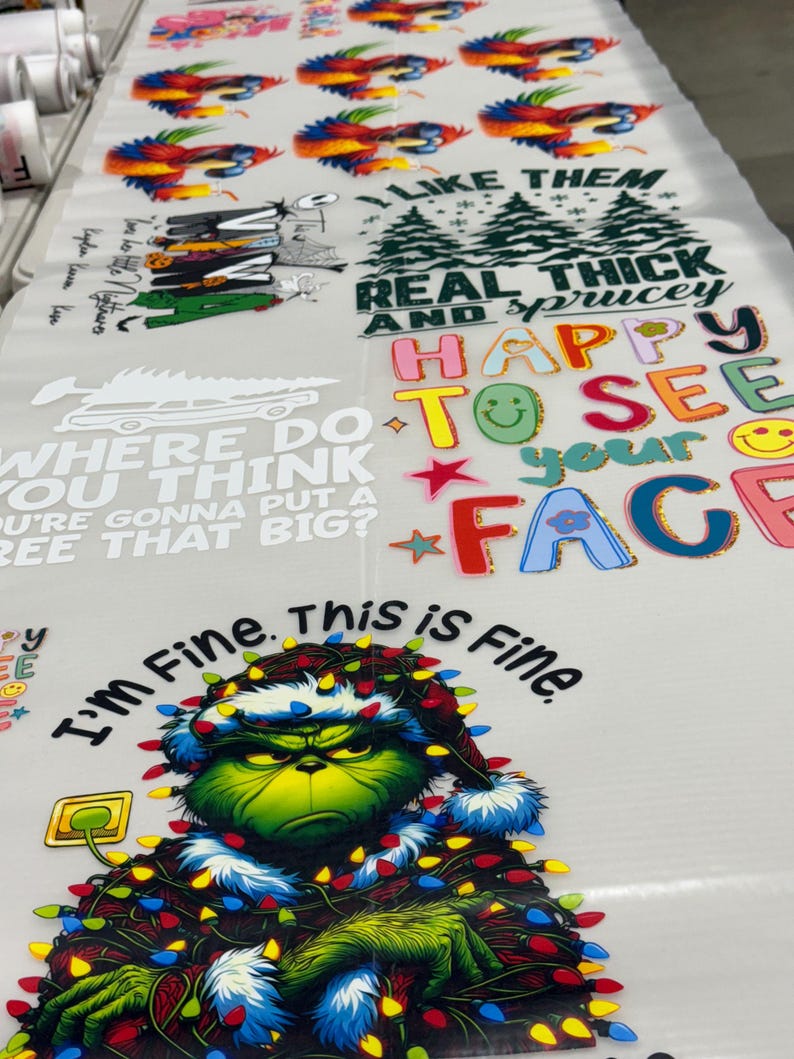 May include: A sheet of printed designs featuring various graphics and text. Designs include colorful birds, Christmas-themed text, and a Grinch character with the text "I'm Fine. This is Fine."