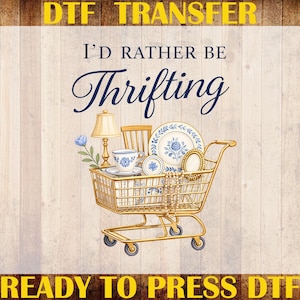 Op de afbeelding: Een DTF-transferontwerp met een gouden winkelwagentje vol vintage items, zoals een lamp, een theekopje en borden. De tekst "I'd Rather Be Thrifting" staat in sierlijke letters. Het ontwerp bevat "Custom Print" en "Ready to Press DTF".
