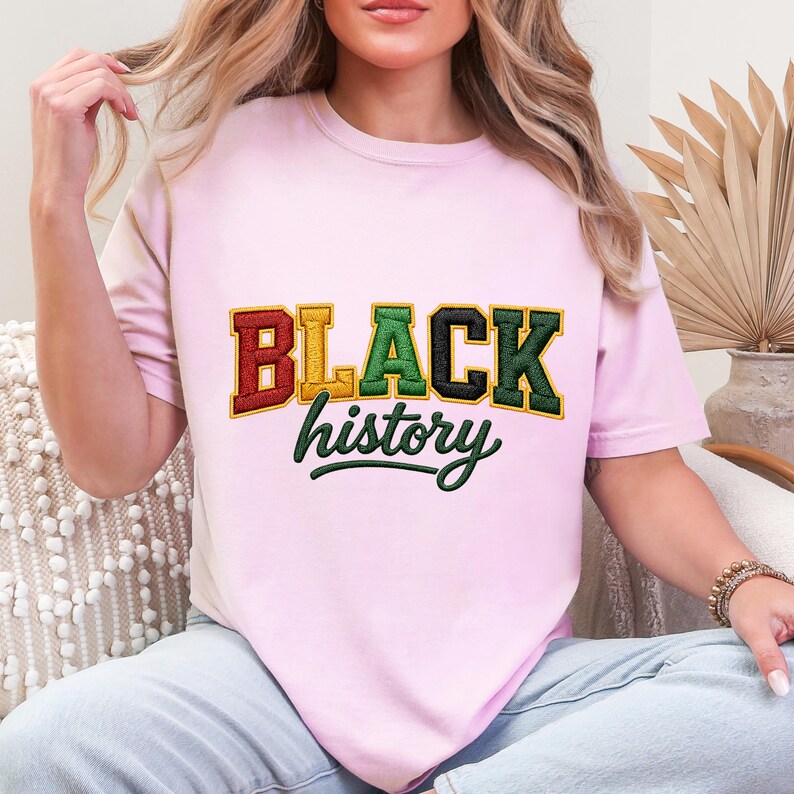 May include: A light pink t-shirt with the words "BLACK history" in a collegiate style. The word "BLACK" is in red, gold, green, and black. The word "history" is in a green script font.